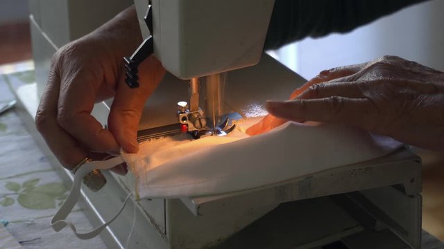 Italy , Milan - Old lady 70 years old sews homemade masks with a sewing machine during n-covid 19 Coronavirus - quarantine at home and lifestyle , seamstress produced masks in her spare time