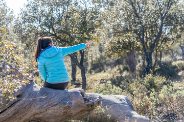 Obraz premium brunette girl with long hair dressed in blue sitting on a dry tree trunk looking at the reflecting field.