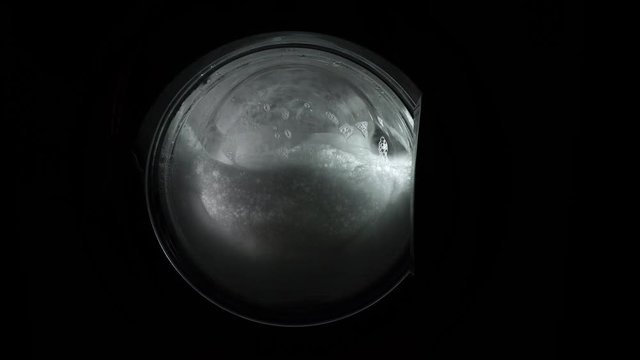 The washing machine on a black, dark background. Spinning drum. The washing process in the washing machine. The problem is with an overdose or the wrong choice of detergent, a lot of foam.