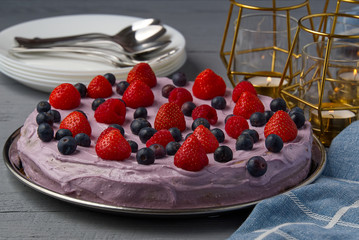 Home made Cheesecake with berries. Cheesecake with Strawberry, blueberry and raspberry on grey wooden table decorated with candles and plates.