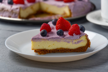 Piece of home made Cheesecake with berries on plate and mug of Americano coffee. Cheesecake with Strawberry, blueberry and raspberry on grey wooden background.