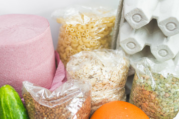 Home food delivery ordered online on white background. Cloth bag with eggs in box, buckwheat, oatmeal, pea porridge, cucumbers, orange and toilet paper. Groceries, donation for coronavirus quarantine.