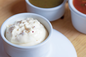spicy garlic sauce in a white bowl against a background of tkemali sauce and satsebeli