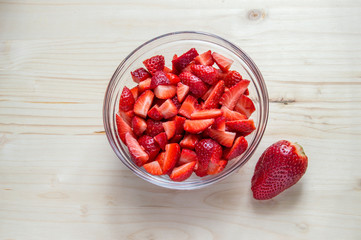 a glass bowl with chopped strawberries isolated on wooden table.