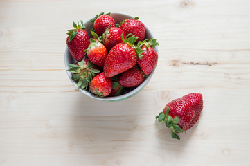 A bowl with strawberries and one outside, isolated on white background