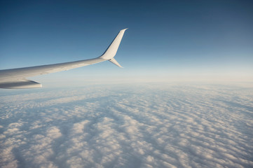 Wing of plane flying over cloudy in the blue sky