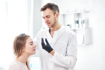 Obraz premium Beautician man gives beauty injections to young woman patient, handsome dermatologist puts botulinum toxin in forehead wrinkles, face filler in the cosmetology salon