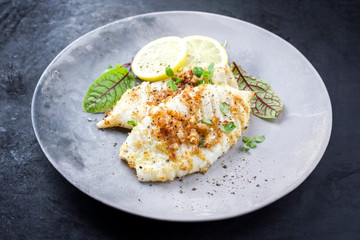 Gebratene Tintenfisch Tuben in Semmelbrösel Panade  mit Zitronen Scheiben und Salat Blätter angeboten als closeup auf einem Modern Design Teller © HLPhoto