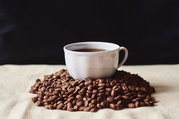 A Cup of espresso coffee drink on a handful of roasted brown coffee beans