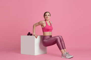 Weights exercises. Beautiful young female athlete practicing in studio, monochrome pink portrait. Sportive fit model training with jump box. Body building, healthy lifestyle, beauty and action concept