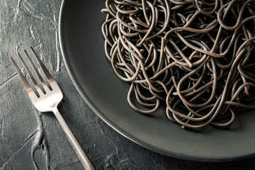 Flat lay of elegant black plate of pasta with sepia ink next to a silver fork with black textured...