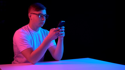 Young man with a smartphone. A man is using a telephone. Blue and red light falls on a man on a black background.