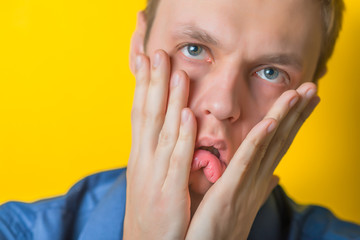 A young man close-up in a blue shirt on a yellow background, showing fatigue two hands face, anger, misunderstanding