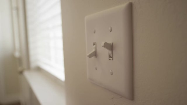 A person turn a light switch on during the day inside a home