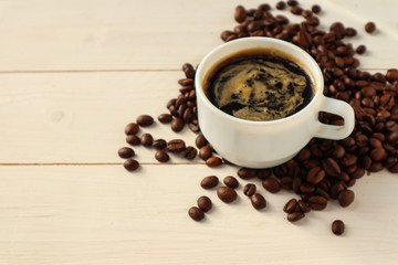 Cup with tasty coffee and roasted grains on wooden table