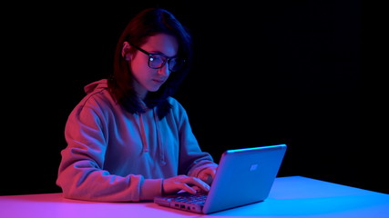 Young woman with a laptop. A woman is using a laptop. Blue and red light falls on a woman on a black background.