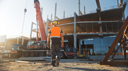 Back Shot of Worker Contractor Wearing Hard Hat and Safety Vests Walks on Industrial Building...