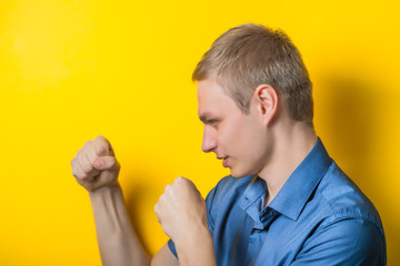 handsome elegant young man wearing a suit posing with fists up gesturing fight isolated on yellow