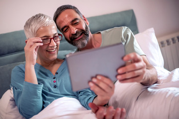 Mature couple using digital tablet in bedroom