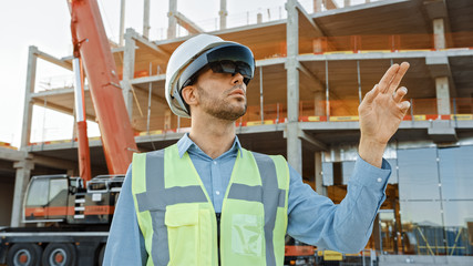 Futuristic Architectural Engineer Wearing Augmented Reality Headset and Using Gestures to Control Commercial Building Construction Site. In Background Skyscraper Formwork Frames and Industrial Crane