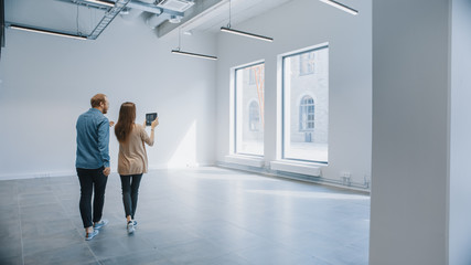 Young Hipster Man and Female Stand in an Empty White Office and Map it with an Augmented Reality...