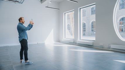 Young Hipster Man in Glasses Standing in Empty Office and Map it with an Augmented Reality Software on a Tablet. Sunlight Shines Through Big Windows.