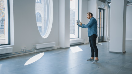 Young Hipster Man in Glasses Standing in Empty Office and Map it with an Augmented Reality Software...