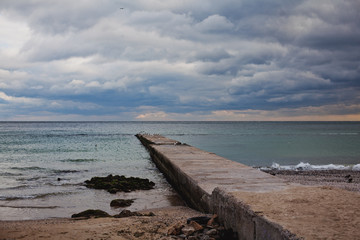 Fototapeta na wymiar Empty beach and gloomy sky, long empty pier, Black Sea