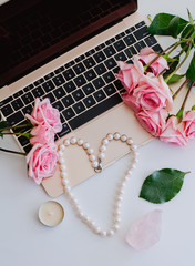 Female workplace with laptop, roses and  pearls. Flat lay, top view