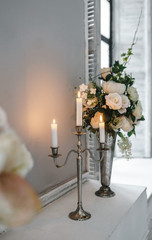 Metal candle holder with burning candles and vases with artificial flowers on a pedestal