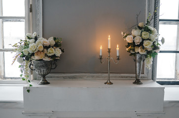 Metal candle holder with burning candles and vases with artificial flowers on a pedestal