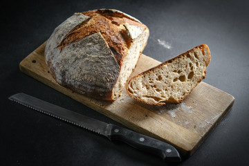 Bread. Homemade sliced whole grain bread on a cutting board with a knife on a dark background copy space.