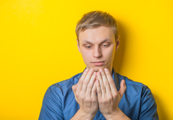 Young man close-up in a blue shirt on a yellow background, reading something or looking at his hands, palms. Mimicry. Gesture. photo Shoot