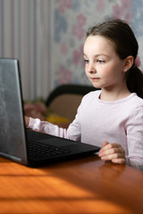 distance learning concept, a little girl sitting at home at a laptop and listening to a lecture.