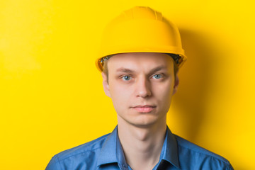 Young man close-up in yellow construction helmet and a blue shirt on a yellow background looking at the camera. Mimicry. Gesture. photo Shoot