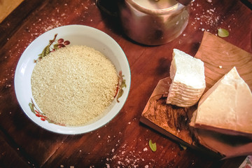 A bowl with chopped pine nuts and some pecorino cheese and parmesan on a wooden board. Preparation of pesto sauce.
