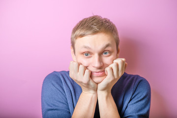 Young man enthusiastically looking at the camera at him, biting his fists. Gesture. On a purple background.