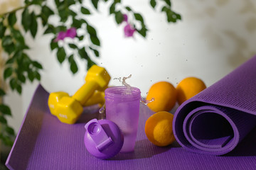 on a lilac yoga mat are yellow dumbbells and a purple glass with fresh water