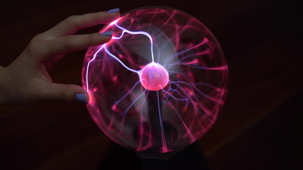 A female hand touches a plasma ball giving out small lightning bolts. Experiments with electricity...