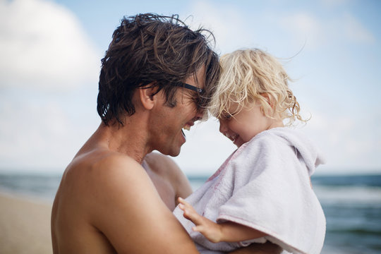 happy cute cheerful girl hugs father by the neck on the beach in summer, dad and daughter relax and play by the sea
