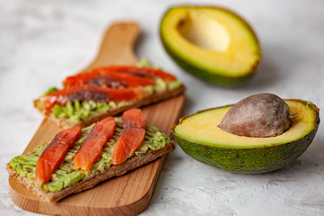 Two sandwiches with red fish and avocado on wooden cutting board