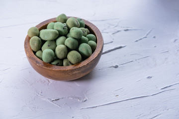 Wasabi peanuts in a wooden bowl on textured white background. Asian snack. Close up view. Copy space.