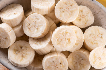 
Bananas cut in a bowl with some bananas in the background