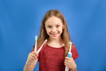 Happy baby girl brushing her teeth with a toothbrush on a blue background. Health care, oral hygiene. Mockup, copy space