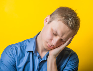 Young man in a blue shirt on a yellow background. wanted to sleep with closed eyes showing fatigue, sleepy, sleepy, hands behind his head. gesture. photo shoot.