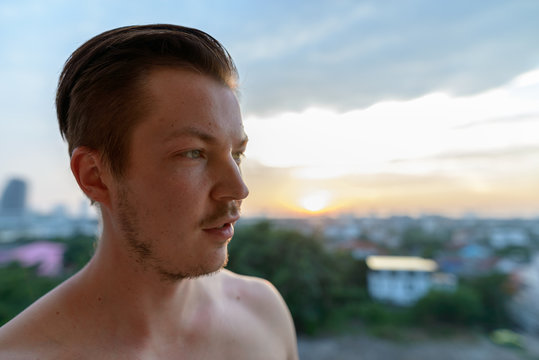 Face of young handsome shirtless man thinking against view of the city