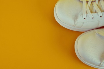 Pair of white shoes on dark yellow background. Trendy summer color.