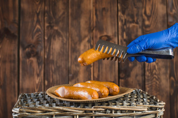 A man in blue protective gloves holds a disposable paper plate with sausages in his hands. He is doing barbecue in the garden party. Free weekend during the Coronavirus epidemic.