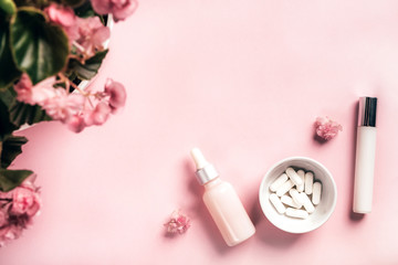 Cosmetic bottles and white capsules with begonia flowers on pink paper background. Health and beauty concept.