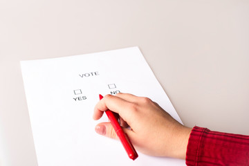 The person fills out the ballot paper. Voting during elections. The photo shows hands, a red pen and ballot paper.
